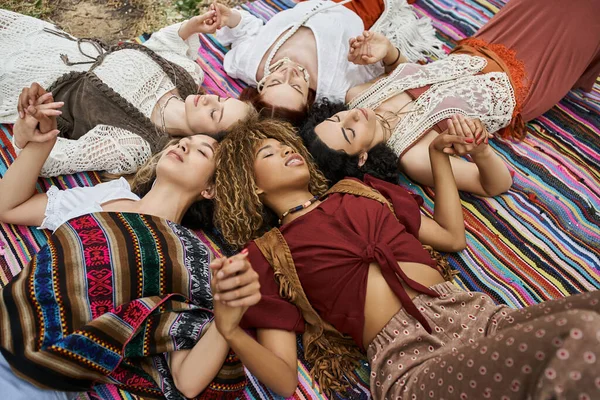 Irklar arası kadınların el ele tutuşup dinlenme merkezinde battaniyeye uzandığı yüksek açılı bir manzara.