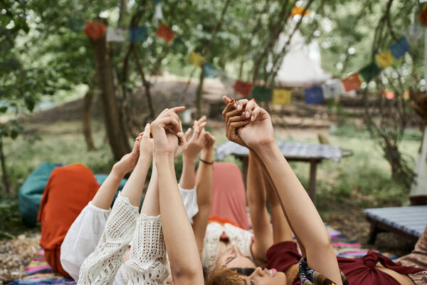 multiethnic women raising and holding hands while lying together outdoors in retreat center
