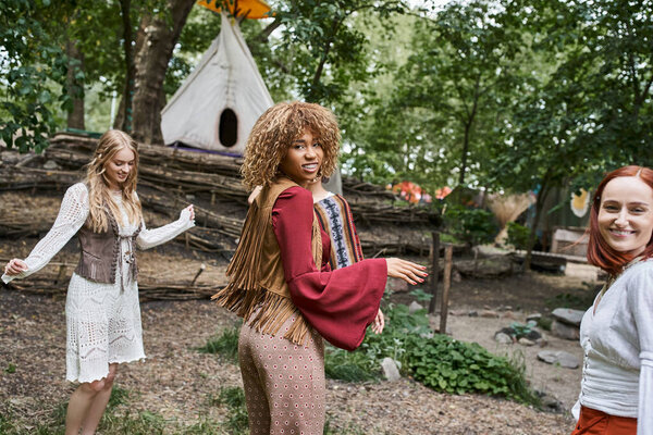 joyful interracial girlfriends in trendy outfits dancing on lawn in retreat center