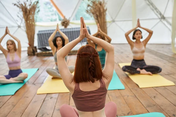 Yoga koçu, inziva merkezindeki çok ırklı kadınlara el kaldırarak poz veriyor.