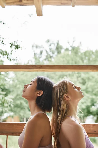 women retreat concept, side view of young girlfriends meditating and relaxing with closed eyes
