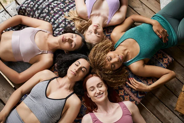 stock image top view of carefree multiethnic girlfriends meditating on pillows with closed eyes, tranquility