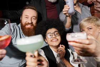 Mutlu sakallı adam ve Afrikalı Amerikalı kadın bardaki iş arkadaşlarının yakınındaki kameraya bakıyor.