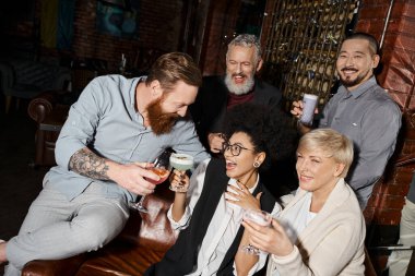 Kokteyl barında çok ırklı arkadaşların yanında neşeli kadınlarla kadeh tokuşturan sakallı adam.