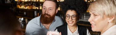 surprised bearded man near cheerful multiethnic women spending after work time in cocktail bar clipart