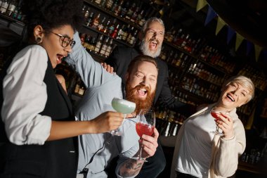 overjoyed multiethnic colleagues with cocktails laughing in bar, diverse team having fun after work clipart