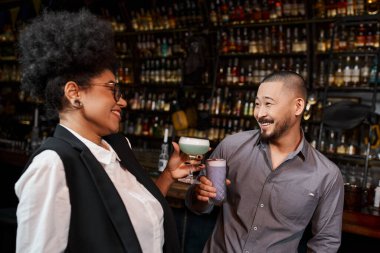 African american woman and asian man with drinks smiling during conversation in cocktail bar, clipart
