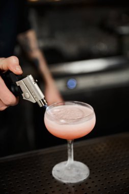 cropped view of bartender using caramelizer while preparing milk punch in bar, cocktail artistry clipart