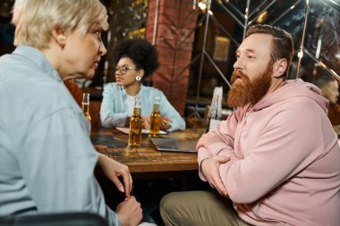 Sakallı adam ve orta yaşlı kadın barda buluşurken Afrika kökenli Amerikalı meslektaşlarının yanında konuşuyorlar.
