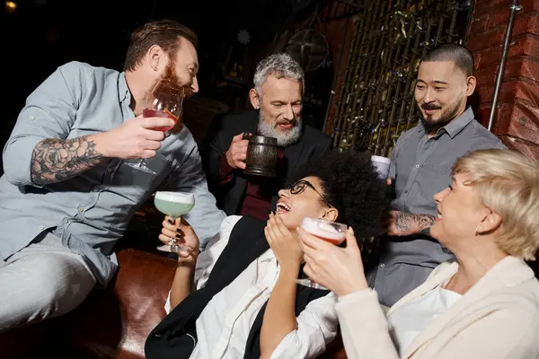 stock image african american woman laughing near multiethnic friends with drinks in bar, after work party
