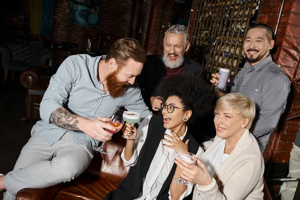 在鸡尾酒吧里 留着胡子的纹身男人在多民族朋友身边与快乐的女人碰杯 — 图库照片