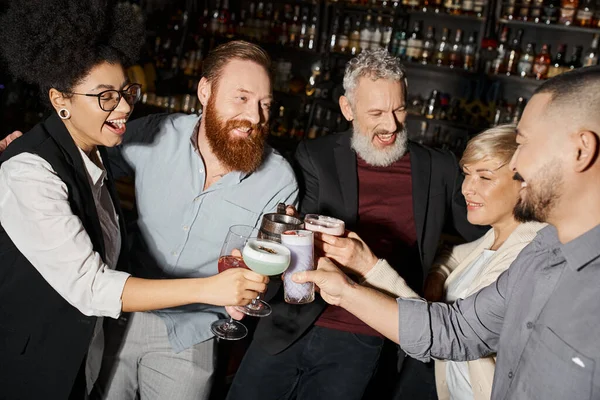 corporate party in cocktail bar, joyful multiethnic colleagues clinking glasses with alcohol drinks
