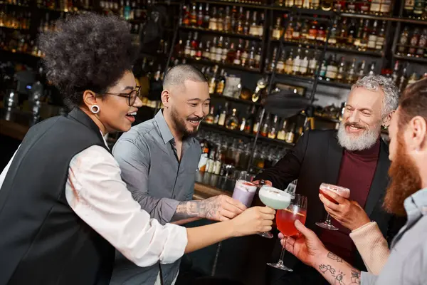 cheerful multicultural work friends clinking cocktail glasses in bar, leisure and fun after work