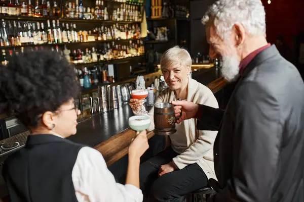 stock image positive multiethnic women and bearded man relaxing in cocktail bar after work, corporate party