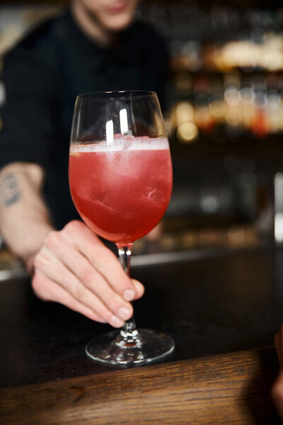 cropped view of bartender holding glass with fruit alcohol cocktail in bar, professional mixologist