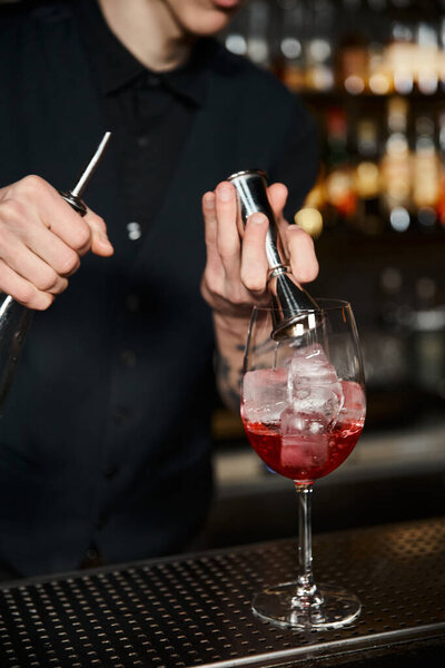 cocktail artistry, cropped view of bartender adding ice cubes in fruit cocktail on bar counter