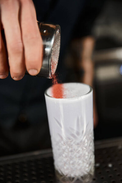 cropped view of bartender adding cinnamon in glass with milk punch, cocktail making in bar ambiance