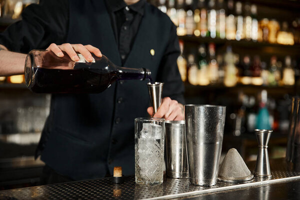 cropped view of bartender pouring alcohol into jigger near glass with ice cubes, cocktail artistry