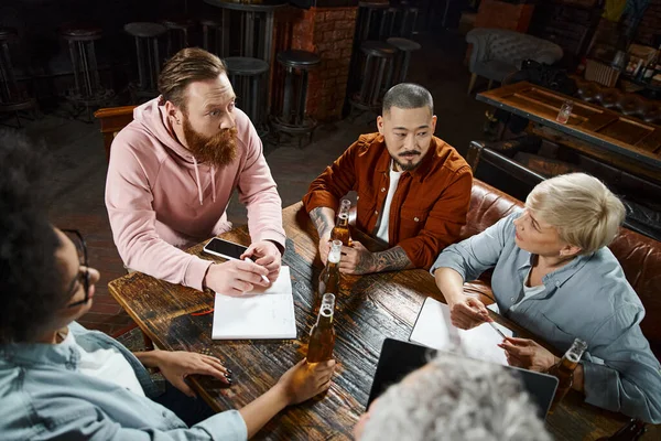 creative team of multiethnic work friends planning new business project while sitting in pub