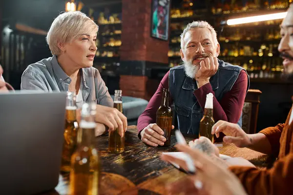 bearded man and middle aged woman listening to asian colleague discussing idea of new project in pub
