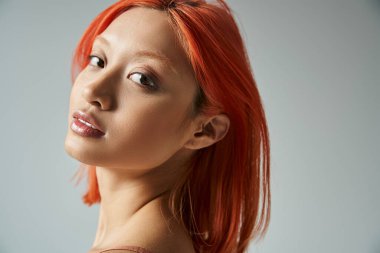 portrait of pretty asian woman with red hair looking at camera on grey background, feminine grace clipart