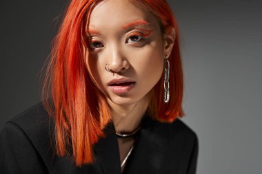 Kırmızı saçlı şık Asyalı model ve gri arka planda piercing pozu, portre