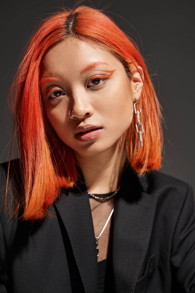 portrait of pretty asian woman with red hair and bold eye makeup looking at camera on grey backdrop