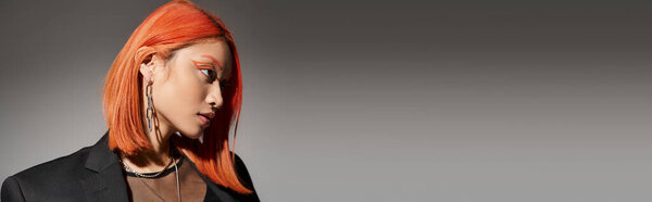 portrait of attractive asian woman with red hair and piercing looking away on grey backdrop, banner
