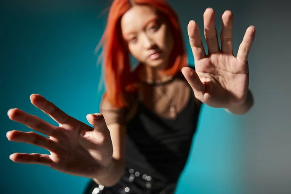 stock image photo with focus on hands, young asian woman with red hair on blurred and blue background,