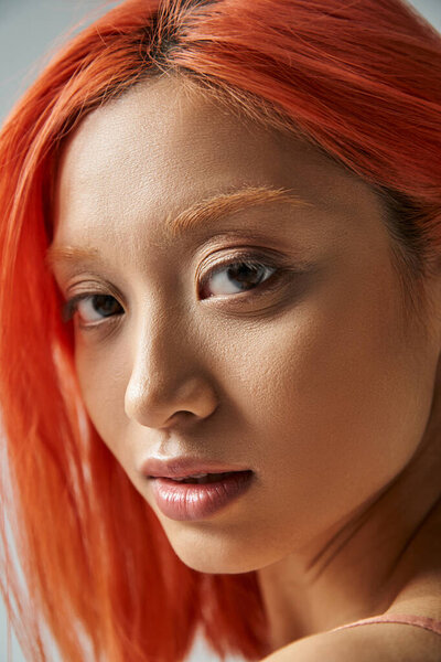 close up of asian young woman with natural makeup and red hair looking at camera, soft skin