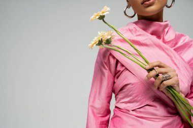 cropped african american woman in pink outfit posing with flowers on grey backdrop, delicate clipart