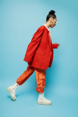 Mavi arka planda yürüyen canlı kıyafetli Afro-Amerikan modeli.