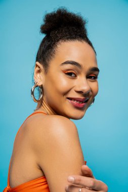 Aksesuarları ve kameraya gülümseyen canlı makyajlı Afro-Amerikan modelinin portresi.