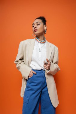 Çekici Afro-Amerikan modeli şık şehir kıyafeti ve turuncu arka planda gümüş yüzükler.