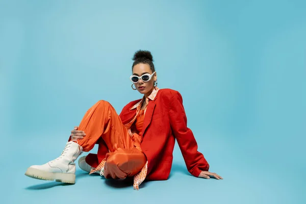 personal style, young african american model in vibrant outfit sitting on blue background