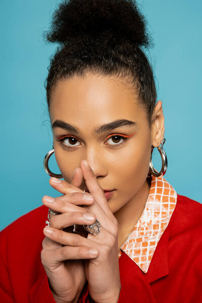 portrait of african american model in silver accessories and vibrant outfit posing on blue backdrop