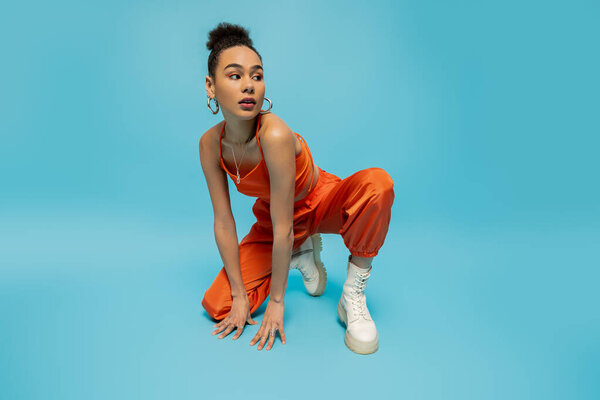 яркая стильная модель, сидящая на одном колене с рукой на полу и глядя в сторону