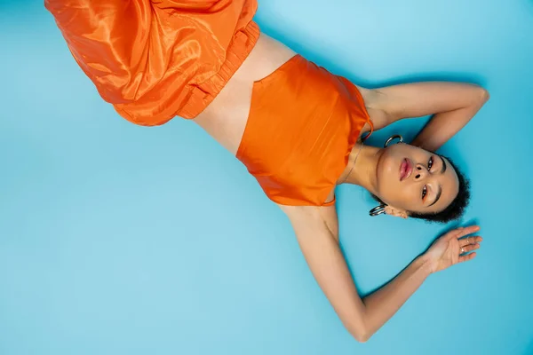 stock image african american woman posing on blue floor wearing bright orange clothing and stylish accessories