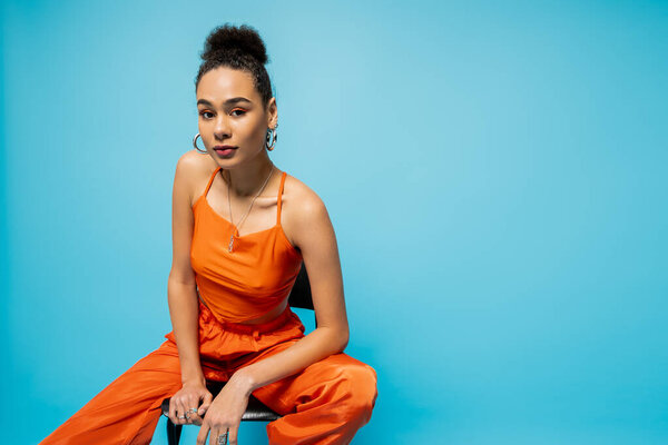 модная модель в модном наряде с аксессуарами, сидящими на высоком стуле и смотрящими в камеру