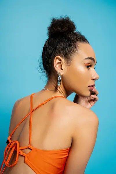 close up back view of attractive african american model in orange trendy outfit looking away