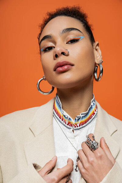 портрет стильной модели в бежевом блейзере, смотрящей в камеру на ярком оранжевом фоне