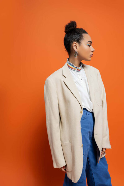 trendy african american fashion model posing in beige blazer and blue pants with accessories