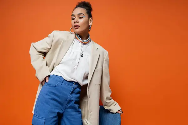 stock image beautiful fashion model in beige blazer and blue pants standing near blue chair and looking away