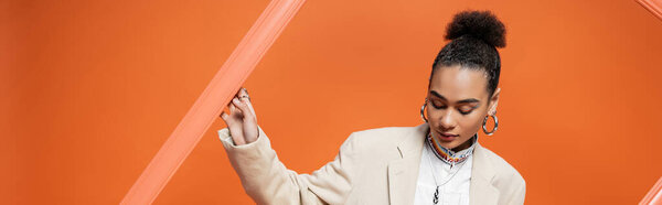 elegant young fashion model in stylish attire with bun and accessories holding orange framework