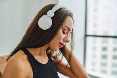Uzun saçlı çekici esmer kadın evde kablosuz kulaklıkla müzik dinliyor.