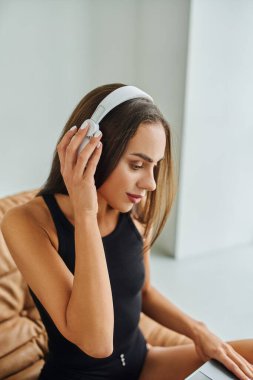 Güzel ve esmer bir kadın. Uzun saçlı. Evde kablosuz kulaklıkla müzik dinliyor.