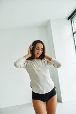 Uzun kollu ve külotlu güzel bir kadın kulaklıkla müzik dinlerken yürüyor.