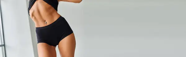 stock image cropped view of sexy slim woman in black sports panties and pierced belly standing at home, banner