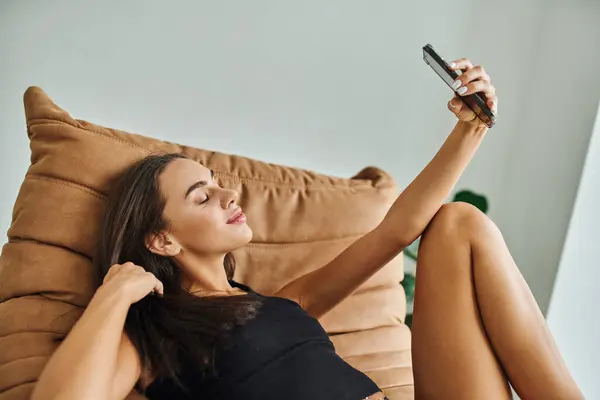 stock image pretty woman in tank top resting on bean bag chair and taking selfie on smartphone, social media