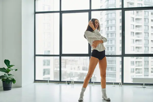 young woman in socks and panties listening music in headphones near panoramic windows at home